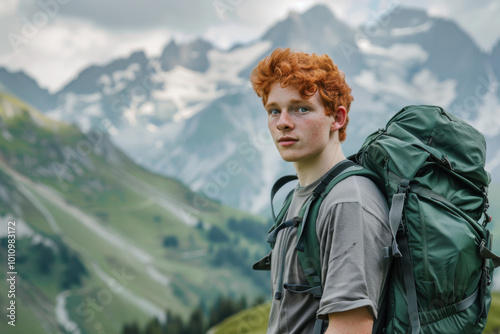 Young man with red hair standing with green backpack. Beautiful mountains on a background. Scenic landscape.