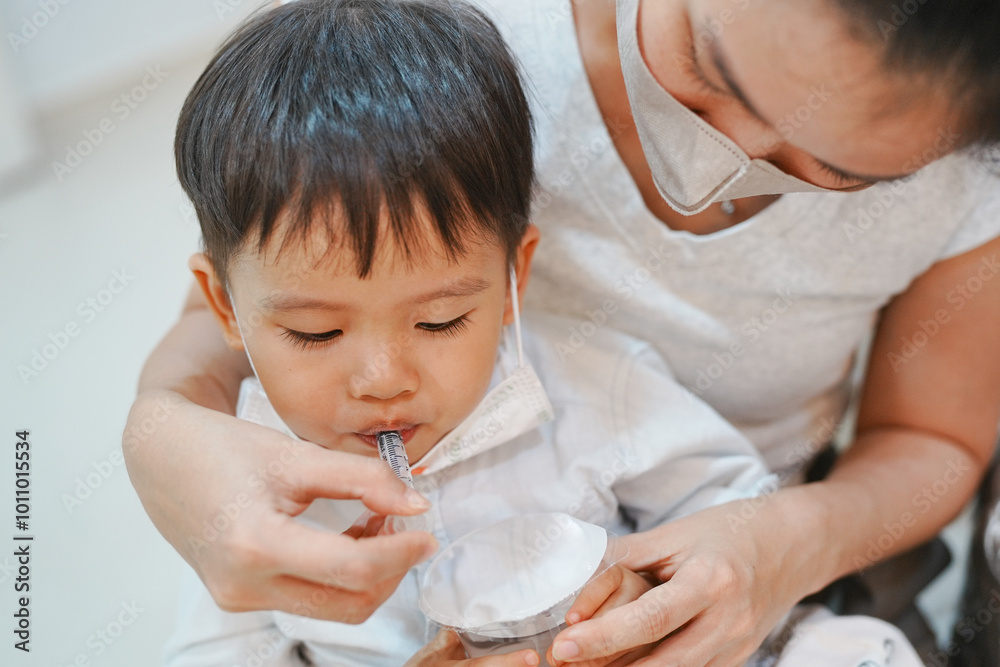 A child drinking with a straw, held by a woman in a mask. Indoor setting, close-up shot highlighting care and safety. A child drinking with a straw, held by a woman in a mask. Indoor setting, close-up shot highlighting care and safety.