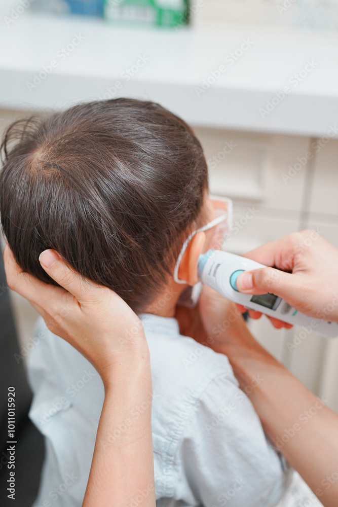 Fototapeta premium Close-up of a thermometer measuring a child's temperature, showcasing health check-up and care at a clinic.