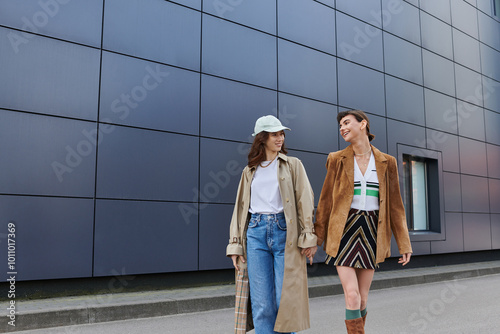 Two young women, dressed in trendy outfits, walk side-by-side on a city street.