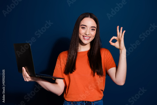 Photo of nice adorable cheerful woman wear orange stylish clothes hold gadget okey sign isolated on dark blue color background