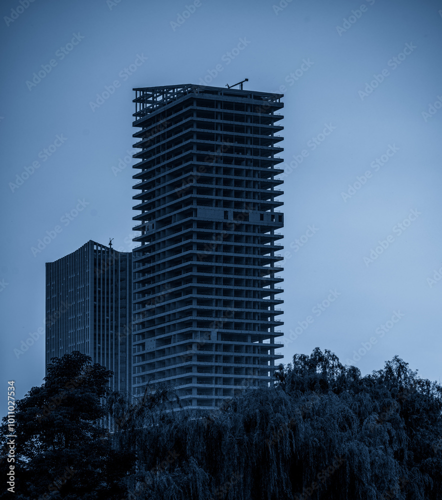 Fototapeta premium Urban Skyscraper Under Construction Surrounded by Lush Greenery