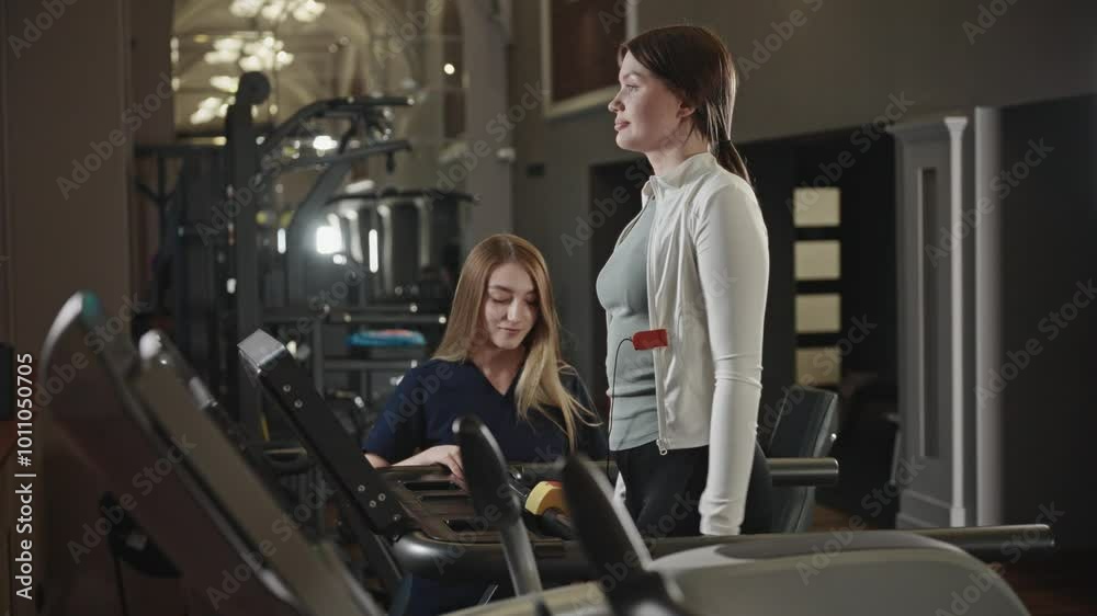 The patient is recovering from an injury using a treadmill in the clinic's specialized gym. A medical professional helps a woman during sports rehabilitation. The patient is recovering from an injury using a treadmill in the clinic's specialized gym. A medical professional helps a woman during sports rehabilitation.