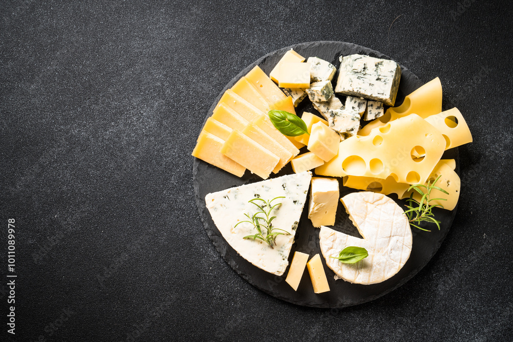 Cheese platter with craft cheese assortment on slate board at black background. Top view with copy space.