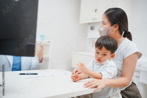 Mother with son at a doctor's office, both wearing masks for safety during a consultation, emphasizing health and protection.