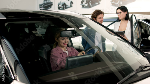 A married couple consults with a female dealer in a modern showroom about their options for a luxury car. This interaction showcases personalized service and expertise in the car-buying experience.