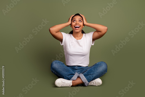 Photo of young lady with ponytail hairstyle sitting floor touch head shocked emotions looking above isolated on khaki color background