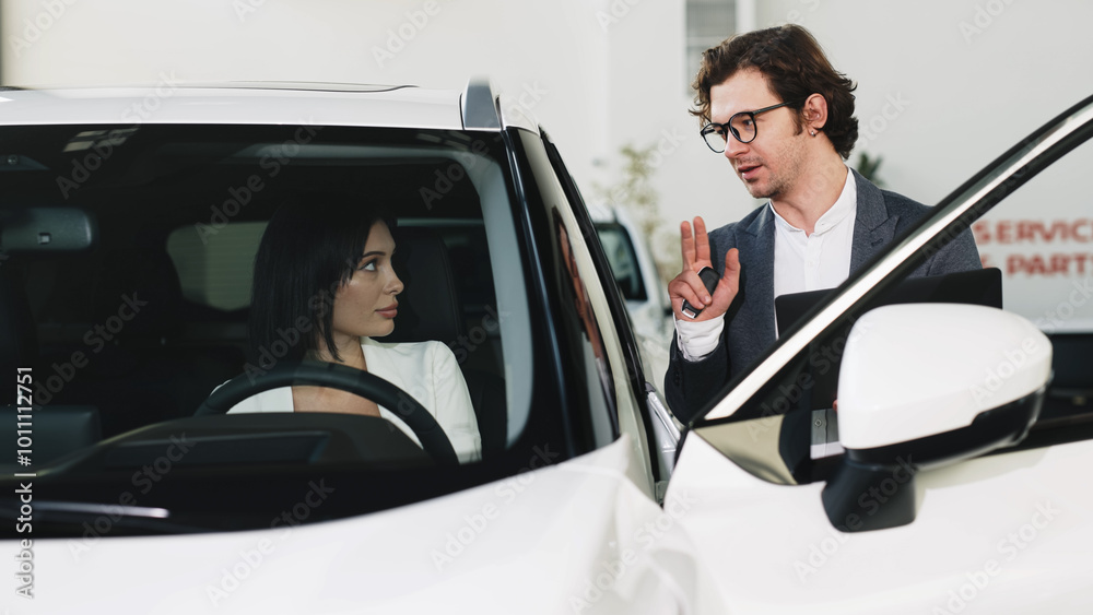 A fashionable young woman inspects a new car at a car dealership while being consulted by a manager. Concept of stylish car purchase or test drive. A fashionable young woman inspects a new car at a car dealership while being consulted by a manager. Concept of stylish car purchase or test drive.