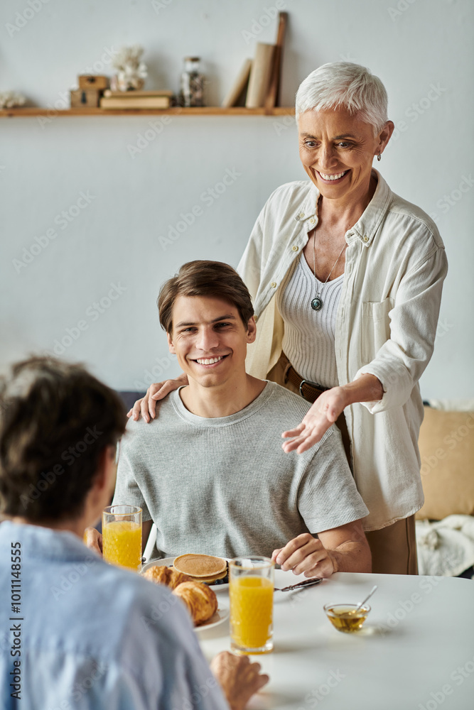 Lesbian parents and their adult son share laughter and love over breakfast in a sunny kitchen. Lesbian parents and their adult son share laughter and love over breakfast in a sunny kitchen.