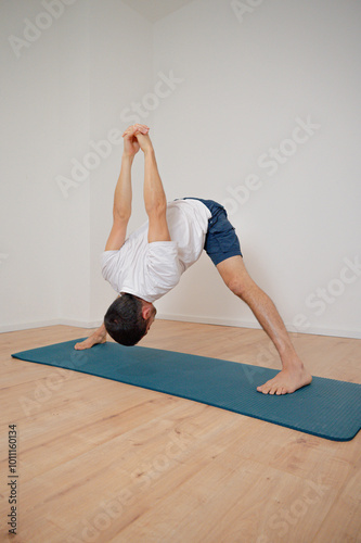 Hispanic man practicing yoga in Prasarita Padottanasana C, a forward bending pose with legs apart. photo