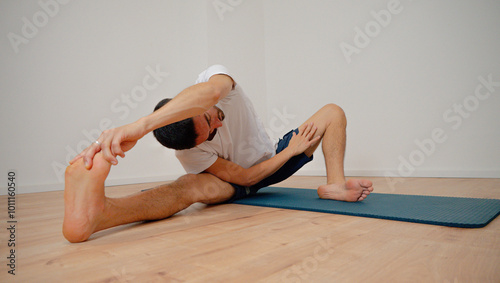 White Latino male performing the open pincer pose (Prasarita Padottanasana) during a yoga session at home, demonstrating strength and balance.