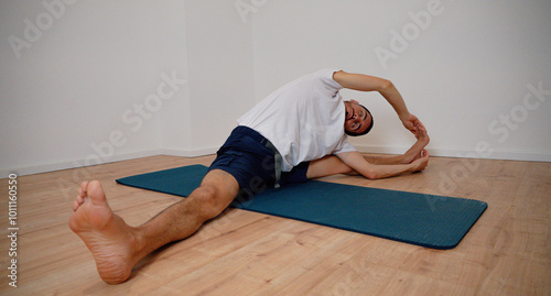 White Latino male performing the open pincer pose (Prasarita Padottanasana) during a yoga session at home, demonstrating strength and balance.