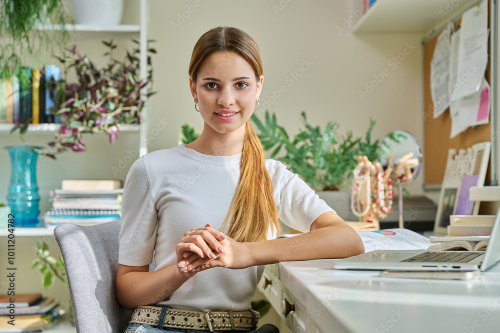 Portrait of smiling female teenager looking at camera, sitting at home at desk with computer Portrait of smiling female teenager looking at camera, sitting at home at desk with computer