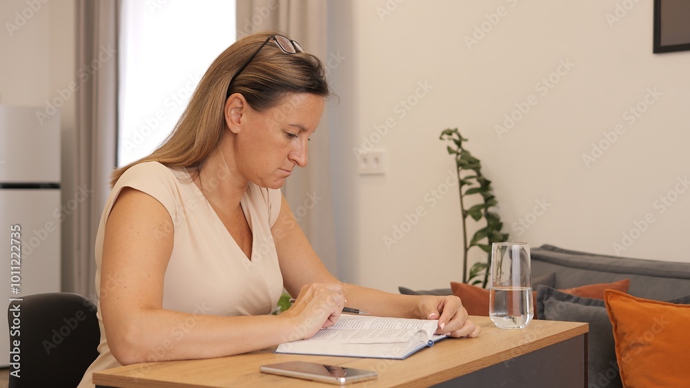 Woman sitting at table writing in notebook, focused on her task. Notebook open, pen in hand, capturing thoughts and ideas. Ideal for themes of productivity, journaling, or notebook use in daily life. Woman sitting at table writing in notebook, focused on her task. Notebook open, pen in hand, capturing thoughts and ideas. Ideal for themes of productivity, journaling, or notebook use in daily life.