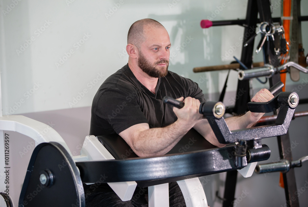 A man is working out on a machine with a black shirt on. He is focused on his workout and he is in a serious mood A man is working out on a machine with a black shirt on. He is focused on his workout and he is in a serious mood