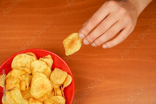 A view of a hand taking potato chips out of bowl. Fast food. Junk food. Unhealthy lifestyle. Calories. Obesity. American food. Hands holds potato chips. Man eating potato chips.