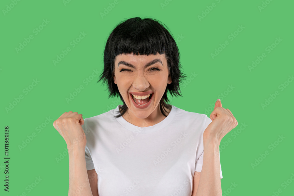 A joyful woman celebrating her success with a big smile and raised fists against a vibrant green background A joyful woman celebrating her success with a big smile and raised fists against a vibrant green background