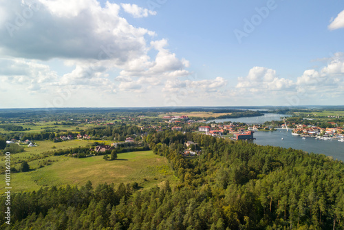 Aerial view of Mikolajskie Lake surrounded by greenery and small towns under a clear blue sky. Perfect for nature lovers and outdoor enthusiasts.