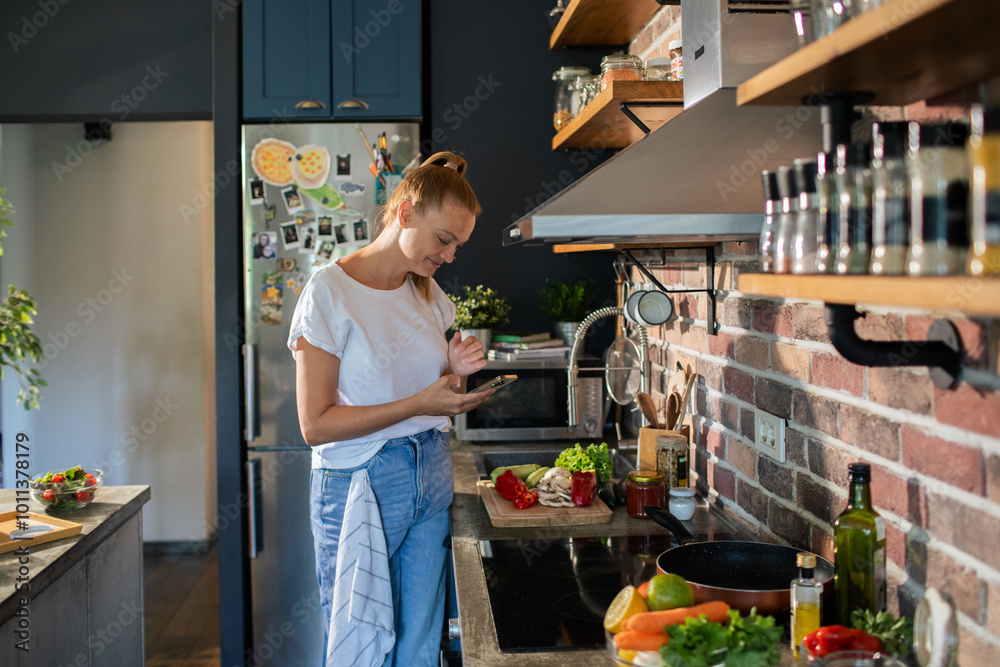 Smiling young woman using smartphone in modern kitchen