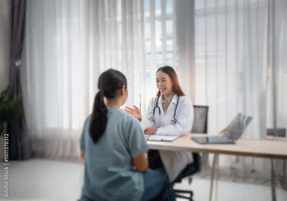 A woman in a white lab coat and stethoscope is sitting at a desk talking to another woman in a blue shirt. A woman in a white lab coat and stethoscope is sitting at a desk talking to another woman in a blue shirt.