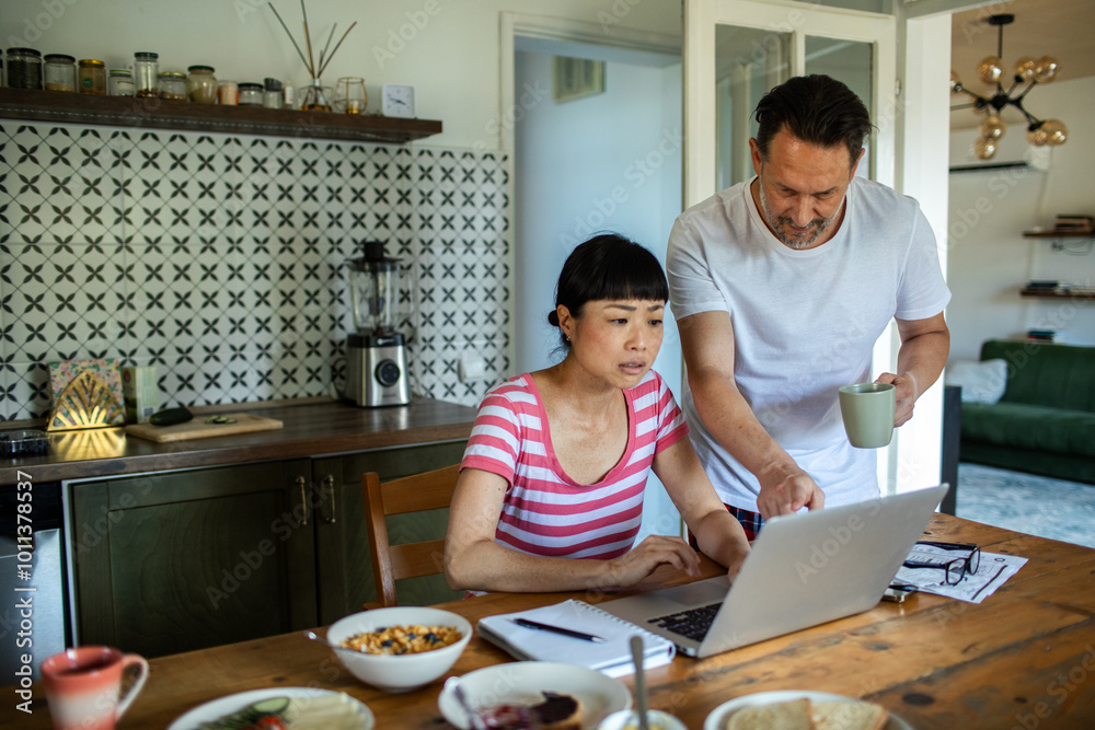 Couple reviewing documents together while using laptop at home Couple reviewing documents together while using laptop at home