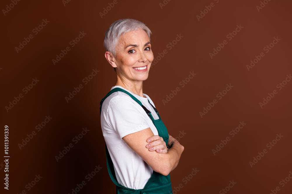 Profile side photo of confident handyman lovely senior woman wear uniform crossed arms isolated on brown color background Profile side photo of confident handyman lovely senior woman wear uniform crossed arms isolated on brown color background