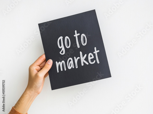 A woman holds a chalkboard with the inscription "go to the market" written in chalk.