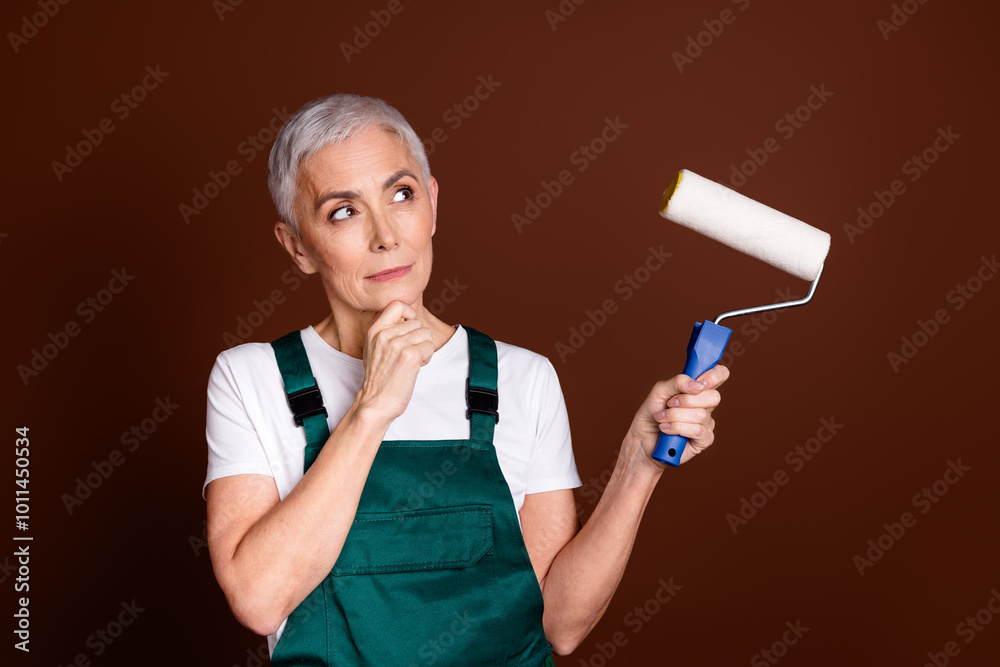 Photo of minded dreamy woman specialist wear green workwear hold brush look empty space isolated on brown color background Photo of minded dreamy woman specialist wear green workwear hold brush look empty space isolated on brown color background