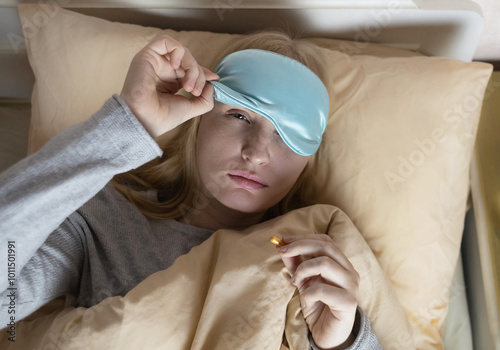 A woman cannot fall asleep and wants to drink a capsule with melatonin, a sleeping pill. Manifestations of jitlag or insomnia. Regulation of biological rhythms