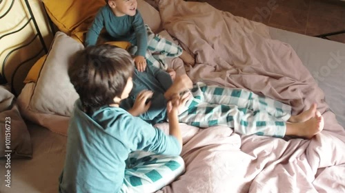 Two children tickling their brother lying on a bed.