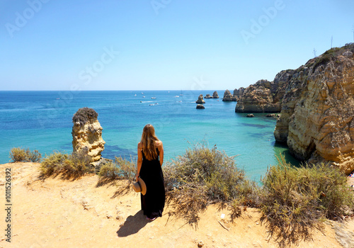 Girl standing on the cliff over a beautiful beach Praia da Dona Ana beach, Lagos, Algarve region in Portugal, summer feeling. background