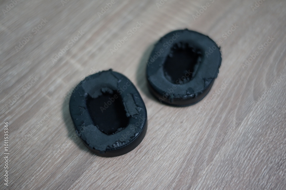 Worn Black Leather Ear Cushions for Headphones on Wooden Surface - Audio Equipment Replacement Parts Close-up Worn Black Leather Ear Cushions for Headphones on Wooden Surface - Audio Equipment Replacement Parts Close-up