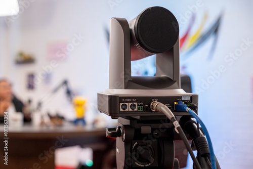 PTZ camera connected with HDMI, 3G-SDI, NDI, and DC12V cables, capturing a livestreaming podcast video in a content creator studio with a blurred background for depth. photo