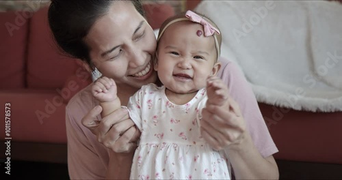 Cute Asian baby girl and mom laughing while playing at home. Candid shot - Mother and child having fun together. Carefree family bond and sweet moment concept.