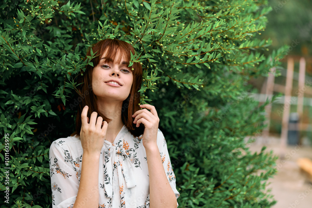 Happy woman in front of bush with hands on head and smiling