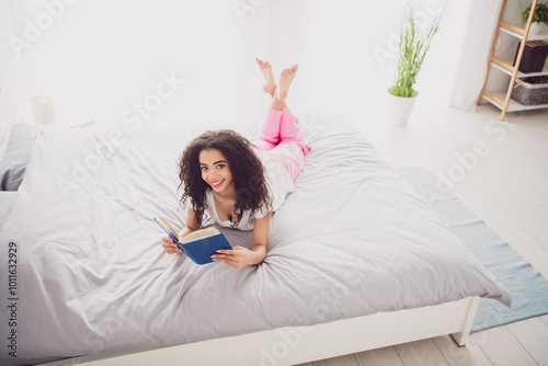 Full size photo of young adorable lady lying bed read book dressed sleepwear chill apartment waking up hotel bedroom white light interior photo