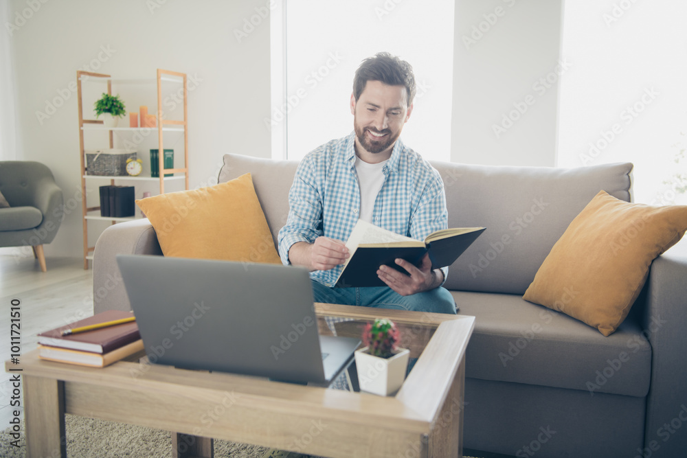 Photo of handsome bearded alone mature age adult man staying home in his new house indoors living room with huge couch reading books Photo of handsome bearded alone mature age adult man staying home in his new house indoors living room with huge couch reading books