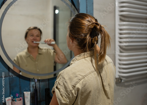 Young woman brushing her teeth in front of a mirror in the bathroom