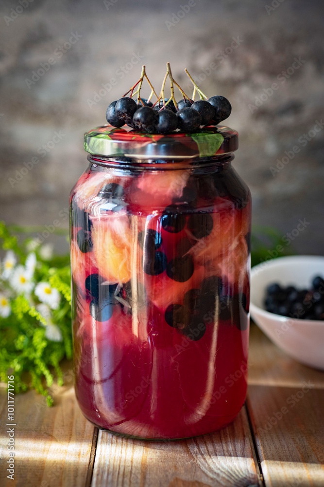 Compote with chokeberry and orange in a glass jar on a gray background. Harvesting for the winter. Vertical photo. Compote with chokeberry and orange in a glass jar on a gray background. Harvesting for the winter. Vertical photo.