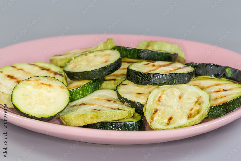 Grilled circles of zucchini and vegetable marrows on pink dish Grilled circles of zucchini and vegetable marrows on pink dish