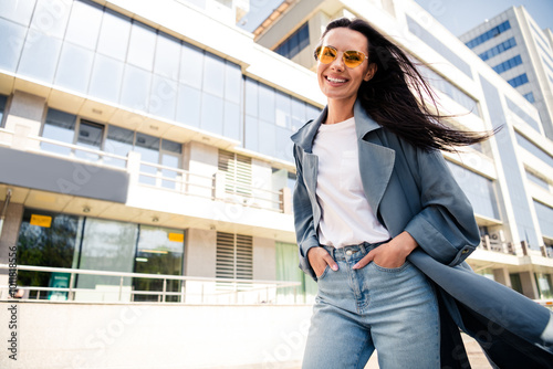 Photo of cheerful pretty lady dressed grey jacket dark eyewear smiling enjoying wind blowing sunshine outdoors town street
