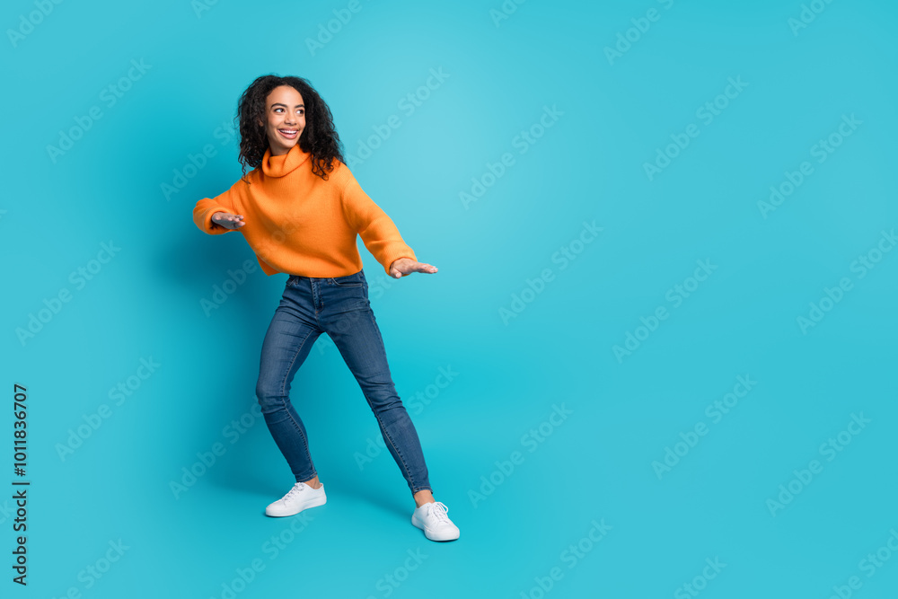 Full length photo of charming positive girl wear orange sweater surfing empty space isolated blue color background Full length photo of charming positive girl wear orange sweater surfing empty space isolated blue color background