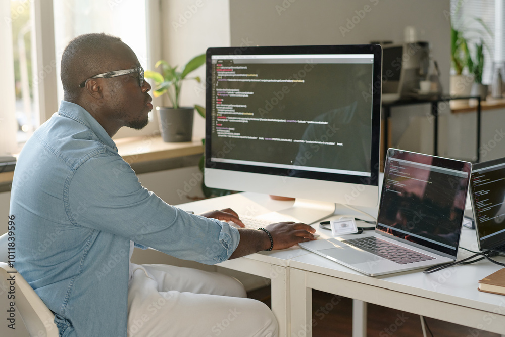 African American man sitting at table and coding in modern office African American man sitting at table and coding in modern office
