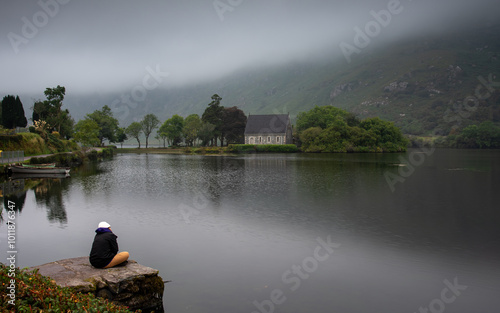 Tourist relaxing by gougane barra lake with saint finbarr's oratory in background on a foggy day photo