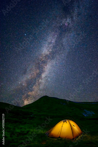 Orange tent lighted from the inside by a flashlight against picturesque starry sky with Milky Way