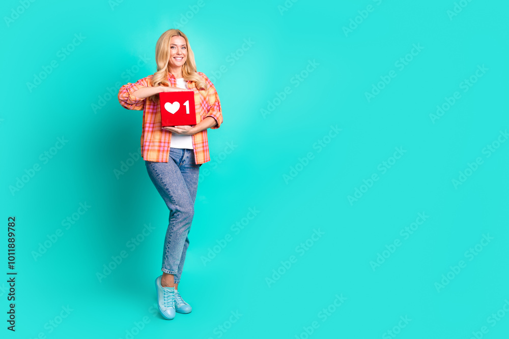 Full body photo of attractive mature woman hold heart icon social media dressed stylish plaid clothes isolated on cyan color background Full body photo of attractive mature woman hold heart icon social media dressed stylish plaid clothes isolated on cyan color background