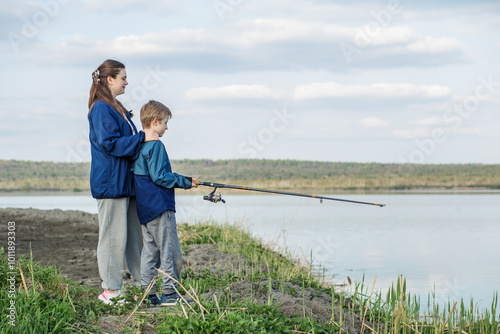 Mother and son fishing together by lake. Family time.