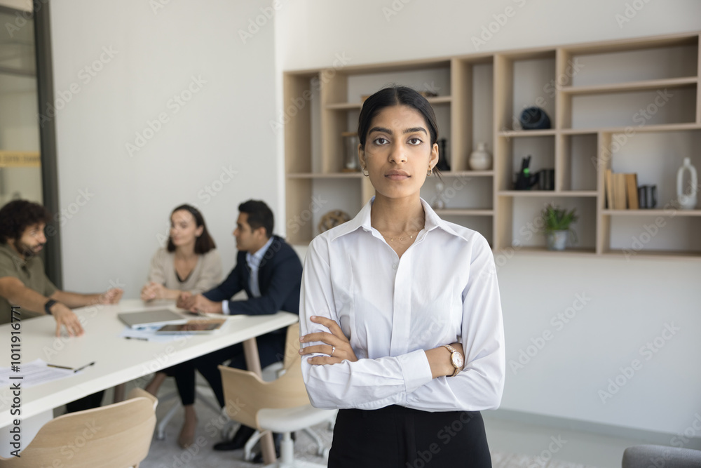 Young Indian lady startup creator pose for portrait while diverse team is engaged in research work develop solution. Female leader represent new business project on top of professional working group Young Indian lady startup creator pose for portrait while diverse team is engaged in research work develop solution. Female leader represent new business project on top of professional working group