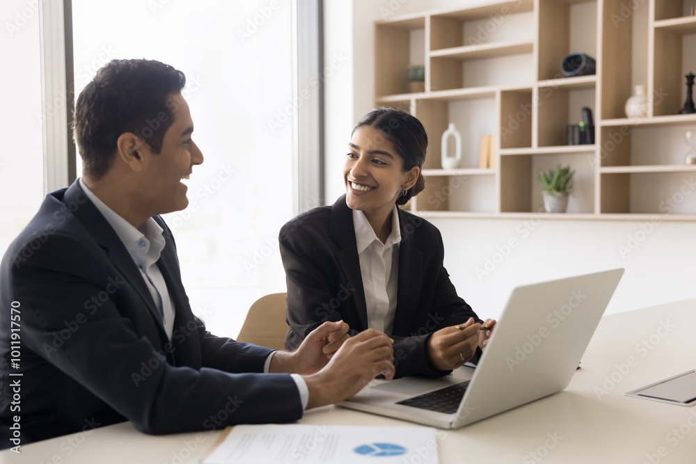 Laughing young Indian executives corporate workers teammates of diverse gender use computer app together enjoy conversation discuss funny work situation. Two colleagues friends having fun on workplace Laughing young Indian executives corporate workers teammates of diverse gender use computer app together enjoy conversation discuss funny work situation. Two colleagues friends having fun on workplace