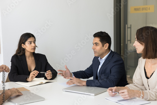 Inspired Indian man corporate worker speak share business plan to colleagues offer sales strategy express idea. Diverse shareholders investors group listen to report of expert on briefing in boardroom photo